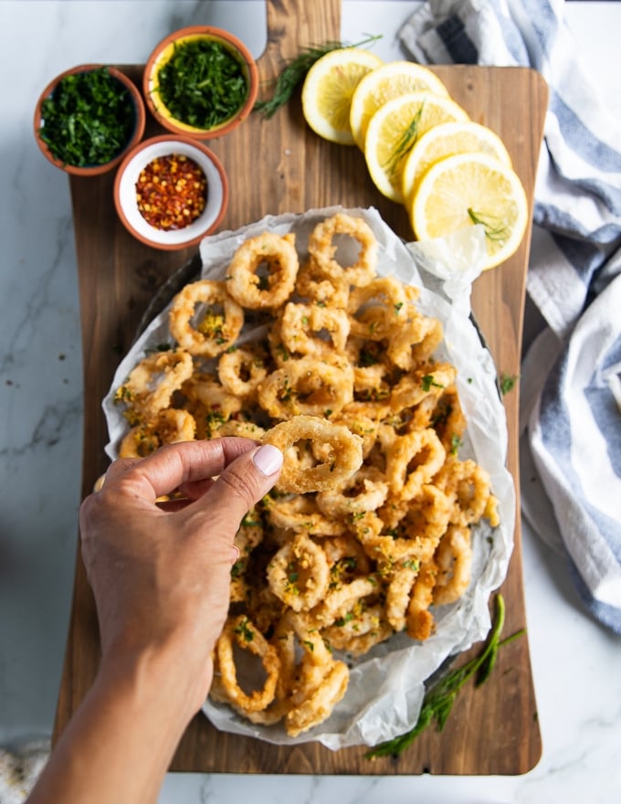 deep-fried calamari on a plate, pictured on a cutting board with dipping sauces. 