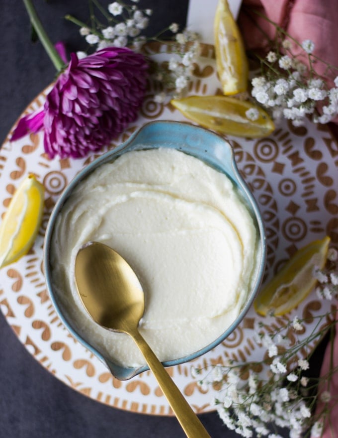 A huge bowl of garlic sauce over a white board surrounded by lemon slices