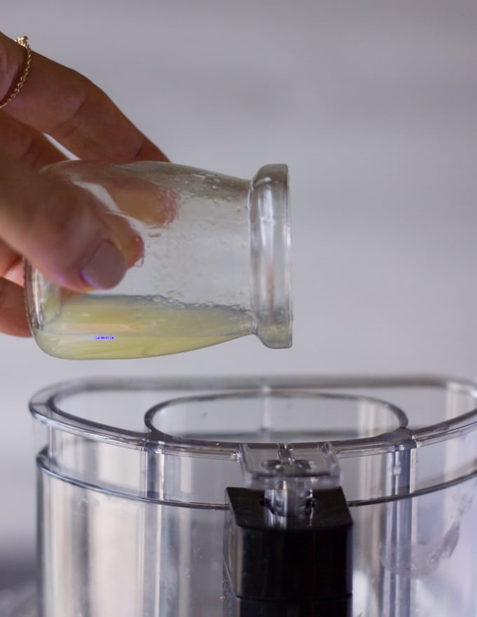 A hand drizzling some lemon juice through the feed tube of a food processor 