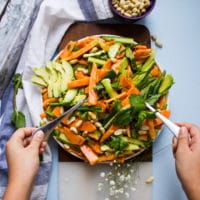 A hand holding two salad spoons tossing the papaya salad withe the dressing