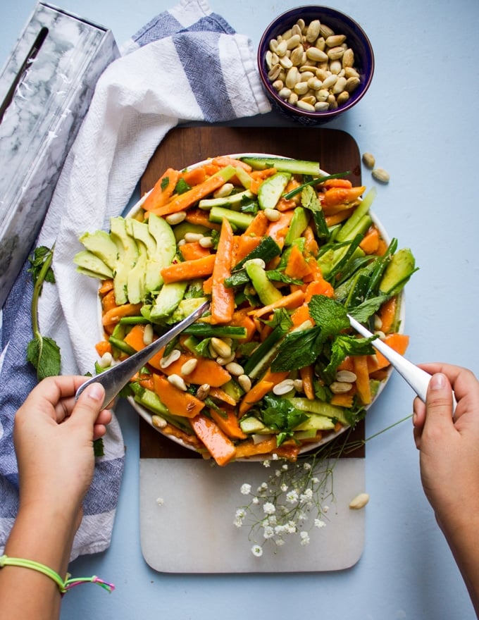 A hand holding two salad spoons tossing the papaya salad withe the dressing 