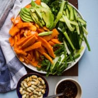 papaya salad recipe ingredients in a bowl including papaya, avocados, cucumbers, scallions, fresh mint, cilantro, a bowl with papaya salad dressing and a bowl of cashews