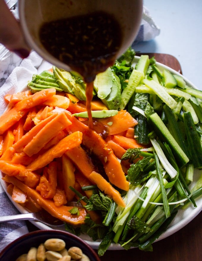 A hand drizzling the papaya salad dressing over the papaya salad recipe