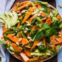 A close up plate of shredded payaya salad with avocados, mint, cucumbers and cashews on a wooden board