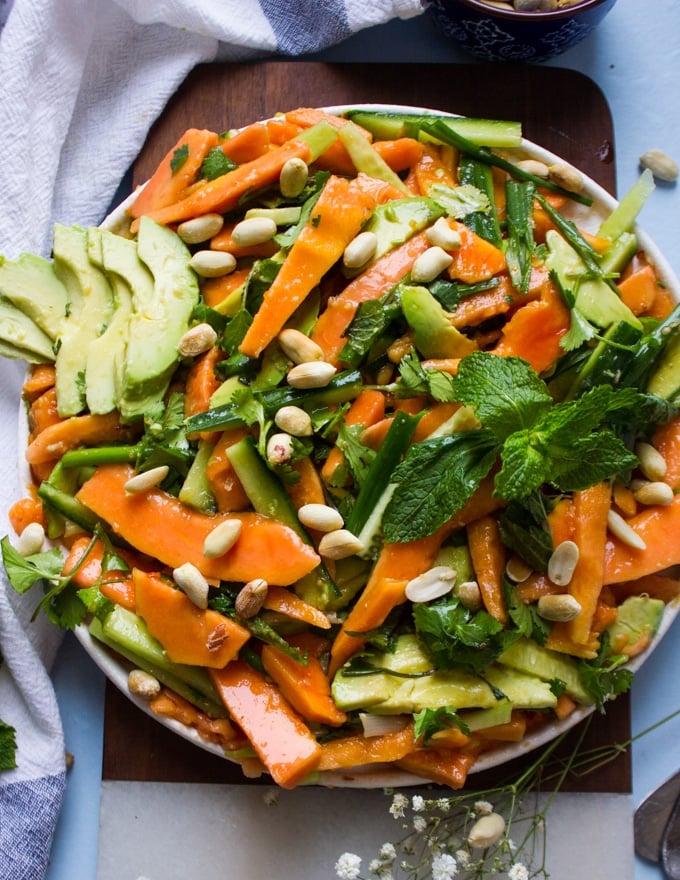 A close up plate of shredded payaya salad with avocados, mint, cucumbers and cashews on a wooden board