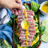 A hand holding a spoon full of mango dressing and drizzling it over the tuna steak recipe