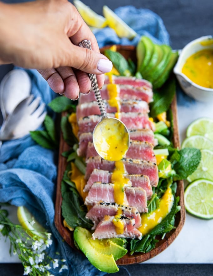 A hand holding a spoon full of mango dressing and drizzling it over the tuna steak recipe 