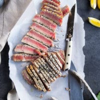 A sharp knife slicing the tuna steak recipe on a board into thin slices showing the rare texture and crispy crust