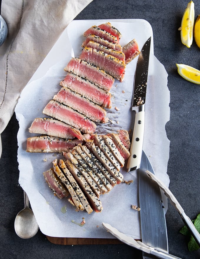 A sharp knife slicing the tuna steak recipe on a board into thin slices showing the rare texture and crispy crust