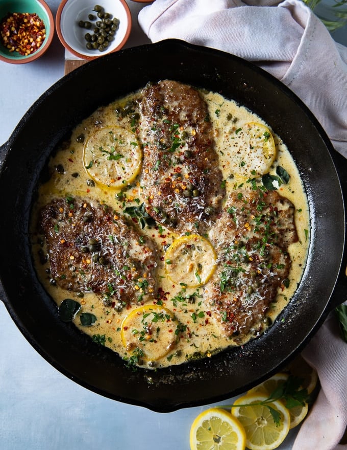 The finished veal scallopini in piccata sauce is ready and garnished with herbs and lemon slices