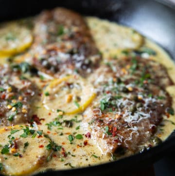 close up of one Veal Scallopini cooked in Piccata sauce in a black pot with lemon slices