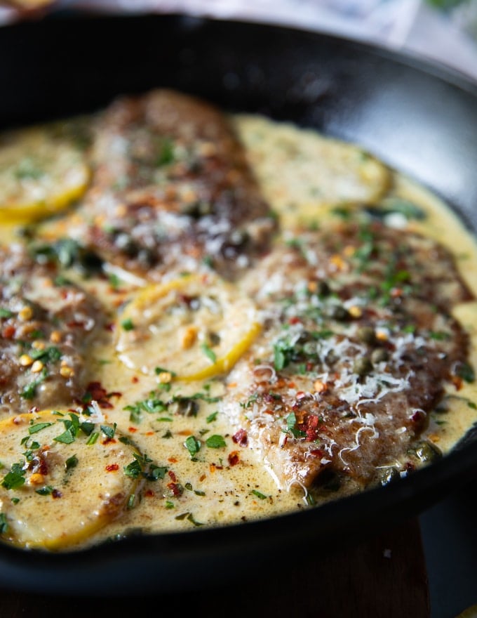 close up of one Veal Scallopini cooked in Piccata sauce in a black pot with lemon slices