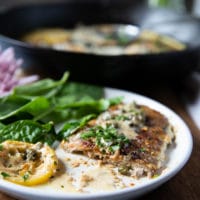 A piece of veal scallopini cur in half on a plate showing the inside of it served with spinach salad