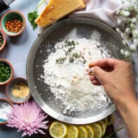 A hand sprinkling some spice on the flour bowl to coat the veal before searing