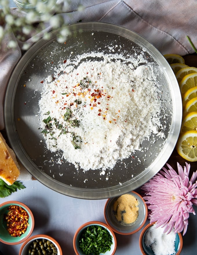 The bowl of flour with fresh herbs, spices and parmesan ready for coating the veal