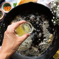 melted butter and garlic cooking in the same cast iron pan and a hand pouring some lemon juice to make the sauce