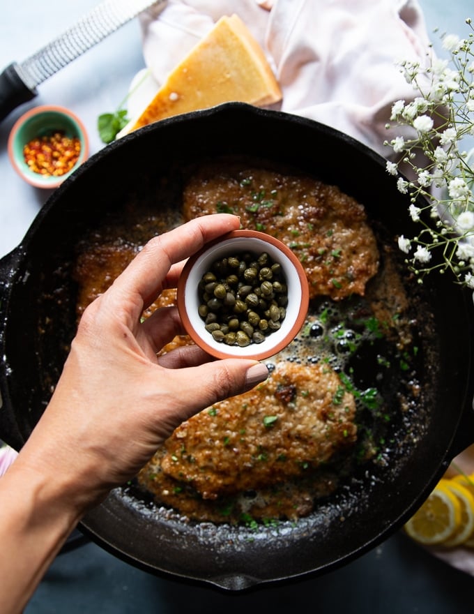 A hand adding in some capers to the piccata sauce 