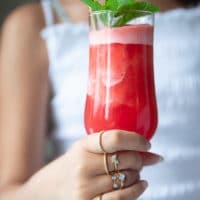 A hand holding a tall cup of watermelon slushie with a mint sprig on top