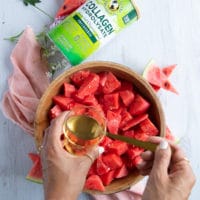 a lage bowl of cubed watermelon and a hand adding the simple syrup to the watermelon