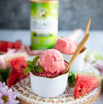 close up of one cup of watermelon sorbet with two scoops in a white bowl and a wooden spoon, and a garnish of mint
