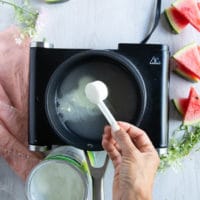 a hand adding in a spoon of collagen to the simple syrup in the pot