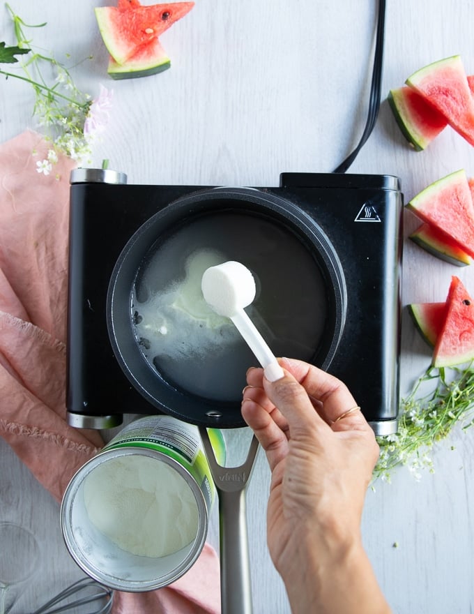 a hand adding in a spoon of collagen to the simple syrup in the pot