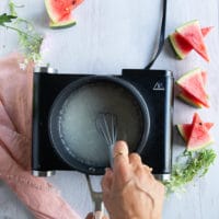 a hand using a whisk to whisk in all ingredients of the simple syrup in a pot until smooth.