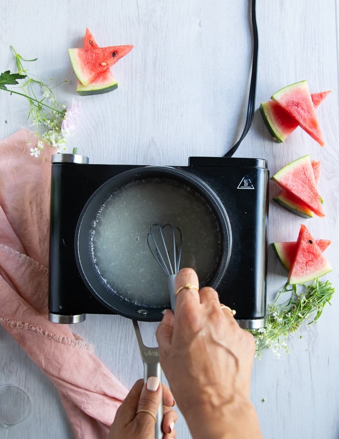 a hand using a whisk to whisk in all ingredients of the simple syrup in a pot until smooth.