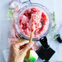 a hand holding off a spoon showing the processed watermelon sorbet recipe over the bowl of food processor