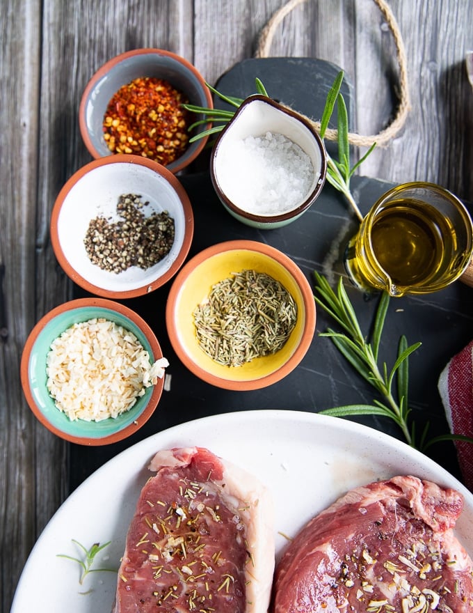 spice blend for NBY strip steak including small bowls of salt, pepper, onion flakes, dried rosemary and olive oil