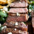 close up of a whole NY strip sliced up and topped with blue cheese crumbles