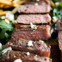 close up of a whole NY strip sliced up and topped with blue cheese crumbles