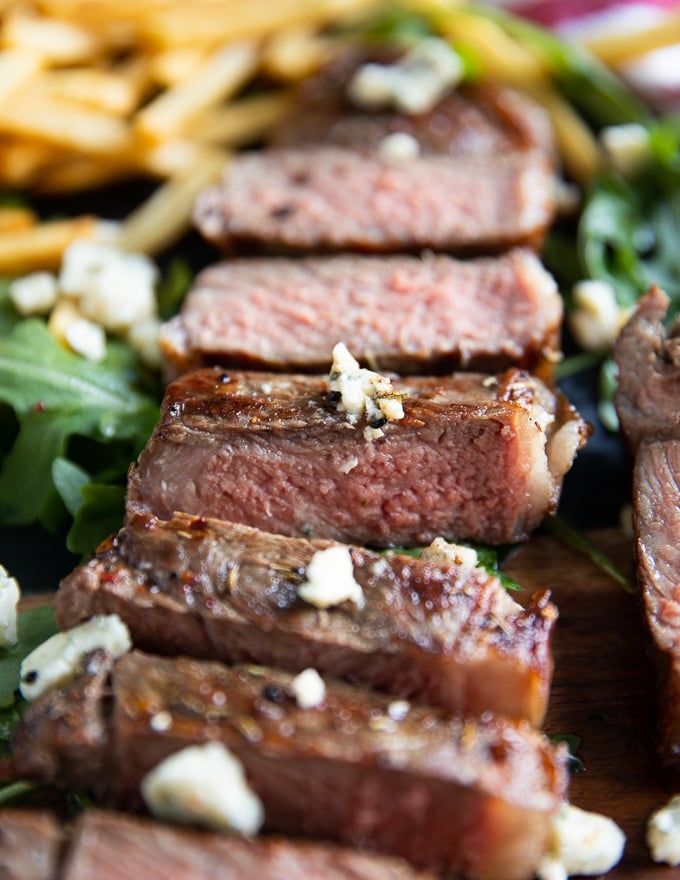 close up of a whole NY strip sliced up and topped with blue cheese crumbles