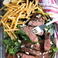 a fork holding a grilled piece of NY strip steak showing how rare and succulent cooked it is