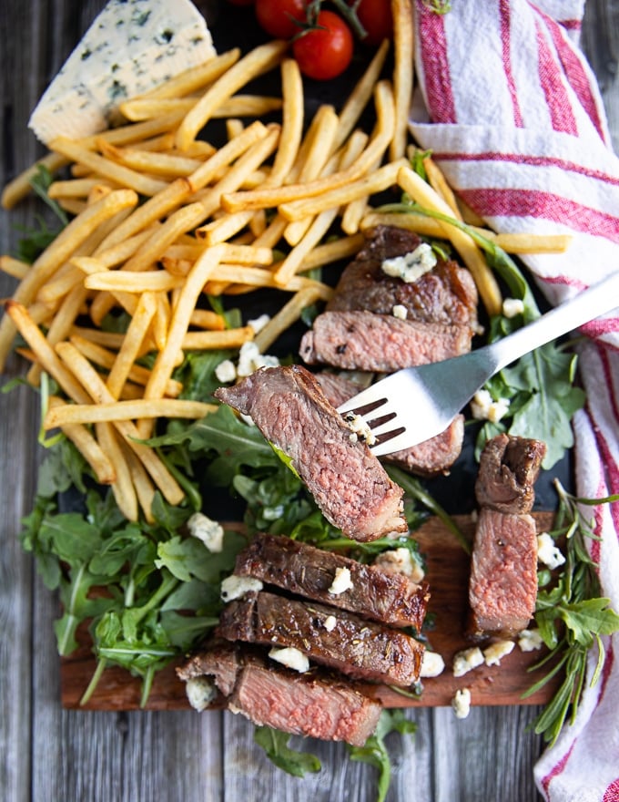 a fork holding a grilled piece of NY strip steak showing how rare and succulent cooked it is