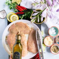 A hand drizzling olive oil over the seasoned chicken breast to make chicken chimichurri