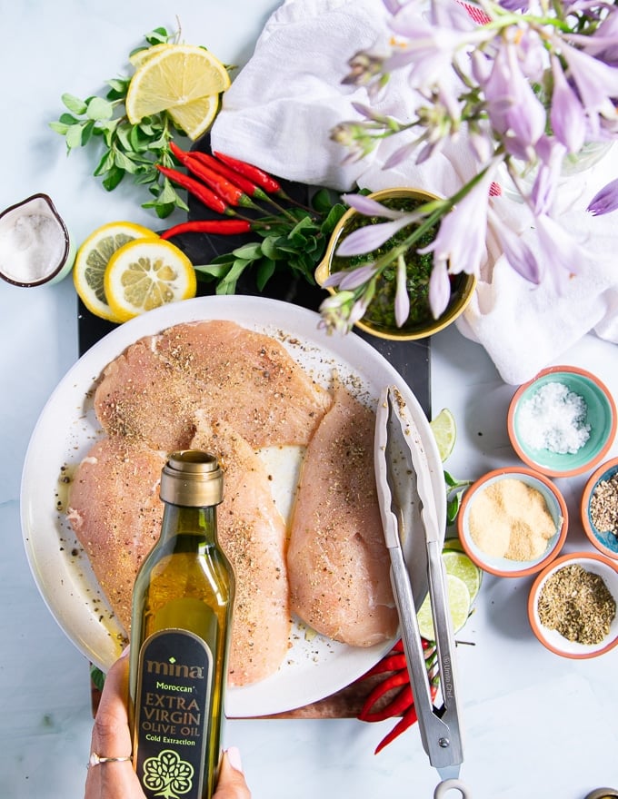 A hand drizzling olive oil over the seasoned chicken breast to make chicken chimichurri