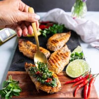 A hand drizzling a lot of chimichurri sauce over grilled chicken to finish off chicken chimichurri