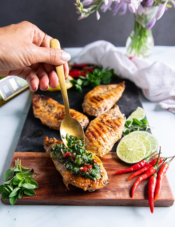 A hand drizzling a lot of chimichurri sauce over grilled chicken to finish off chicken chimichurri