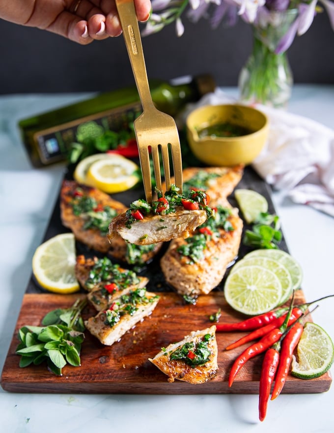 A fork holding off a strip of chicken chimichurri showing how juicy the chicken is and the load of chimichurri sauce over the chicken