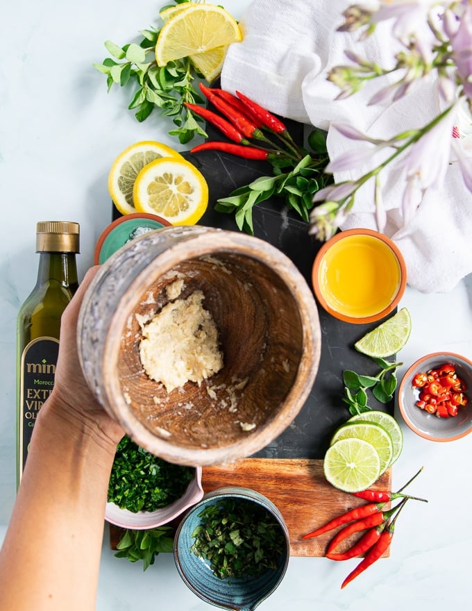 A hand holding a mortar and pestle showing how finely minced the garlic is to make chimichurri sauce