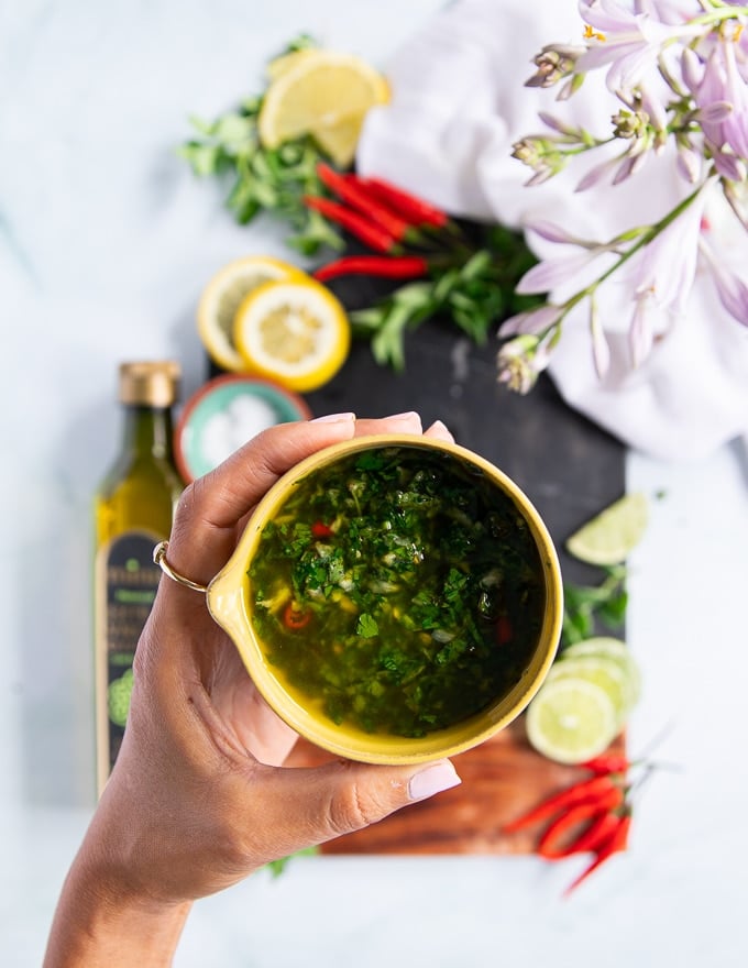 A hand holding a bowl of chimichurri recipe showing the chimichurri sauce in olive oil 