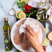 a hand patting down the chicken breasts before seasoning