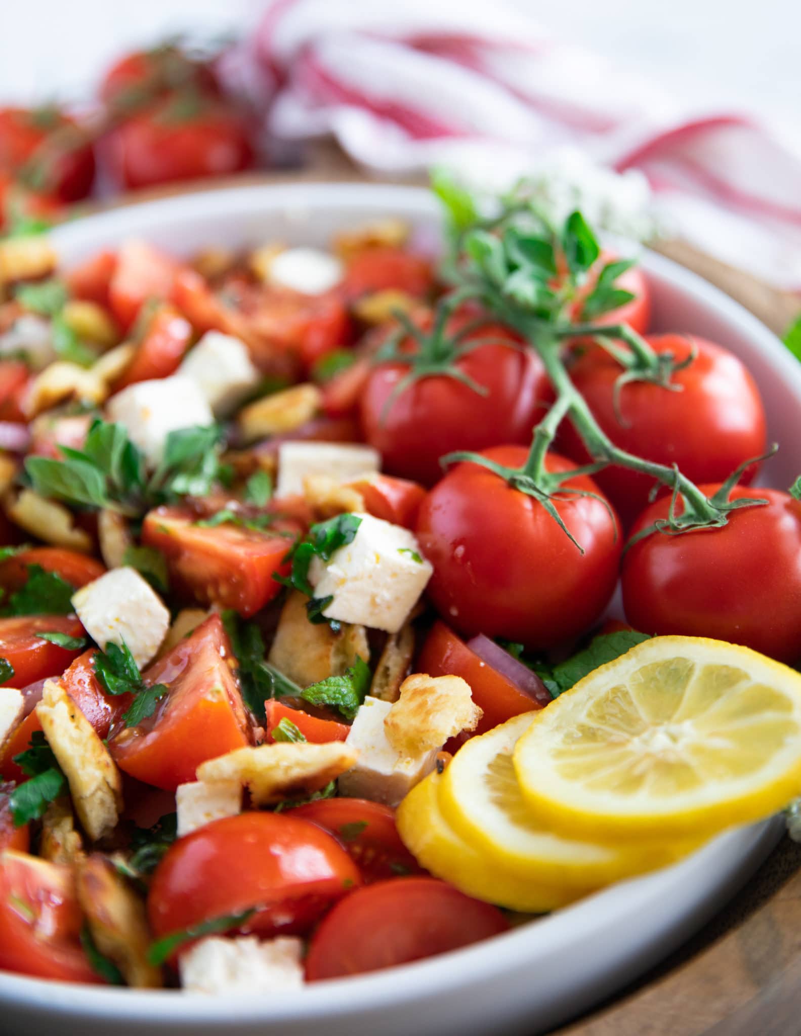 close up of a tomato salad showing the fresh mint, oregano, bread, feta and lemon slices