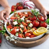 A hand holding a big plate of tomato salad surrounded by a red tea towel