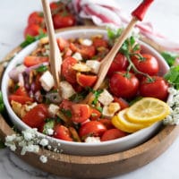 Salad spoons tossing the tomato salad with the simple dressing