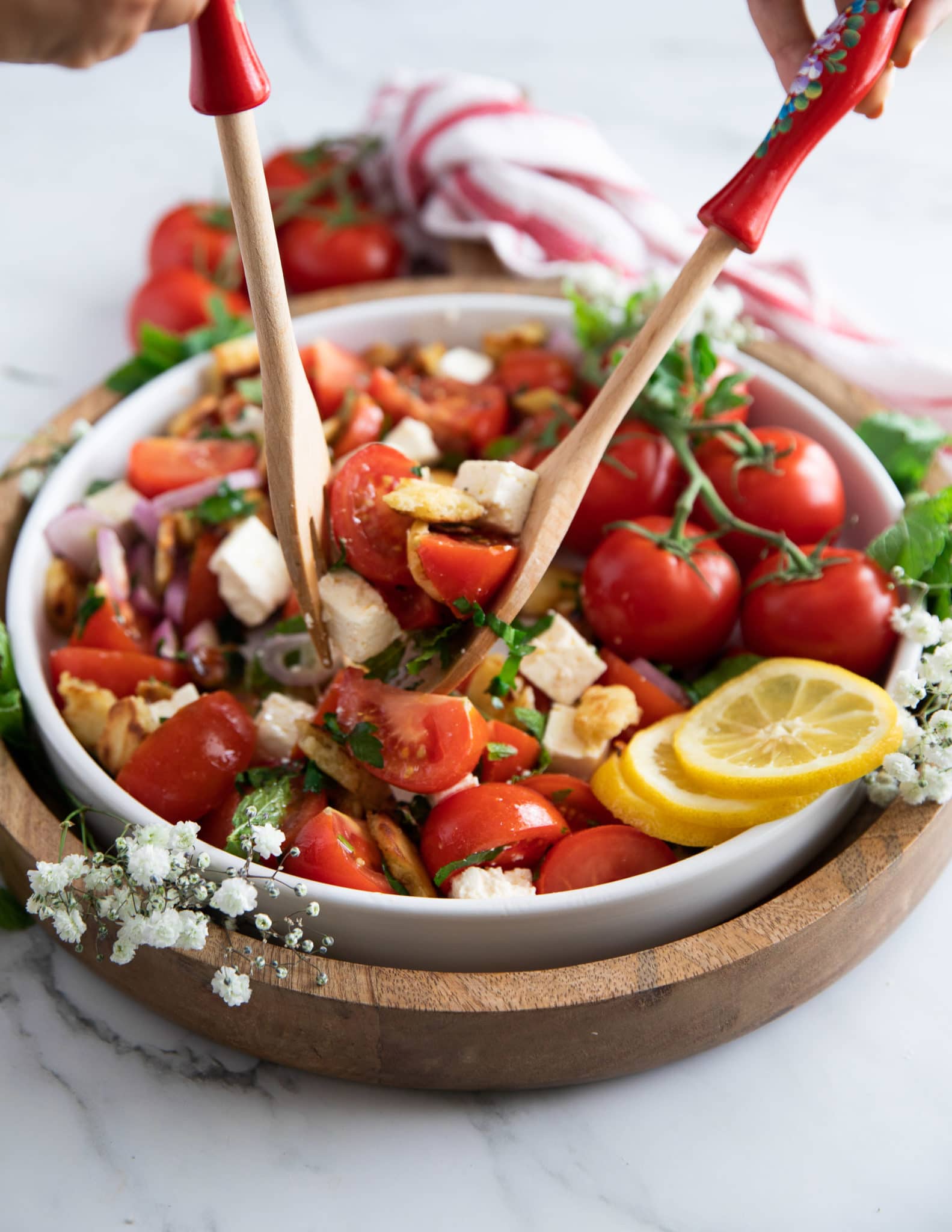 Salad spoons tossing the tomato salad with the simple dressing