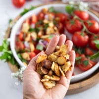 A hand holding the toasted bread chunks ready to toss into the salad