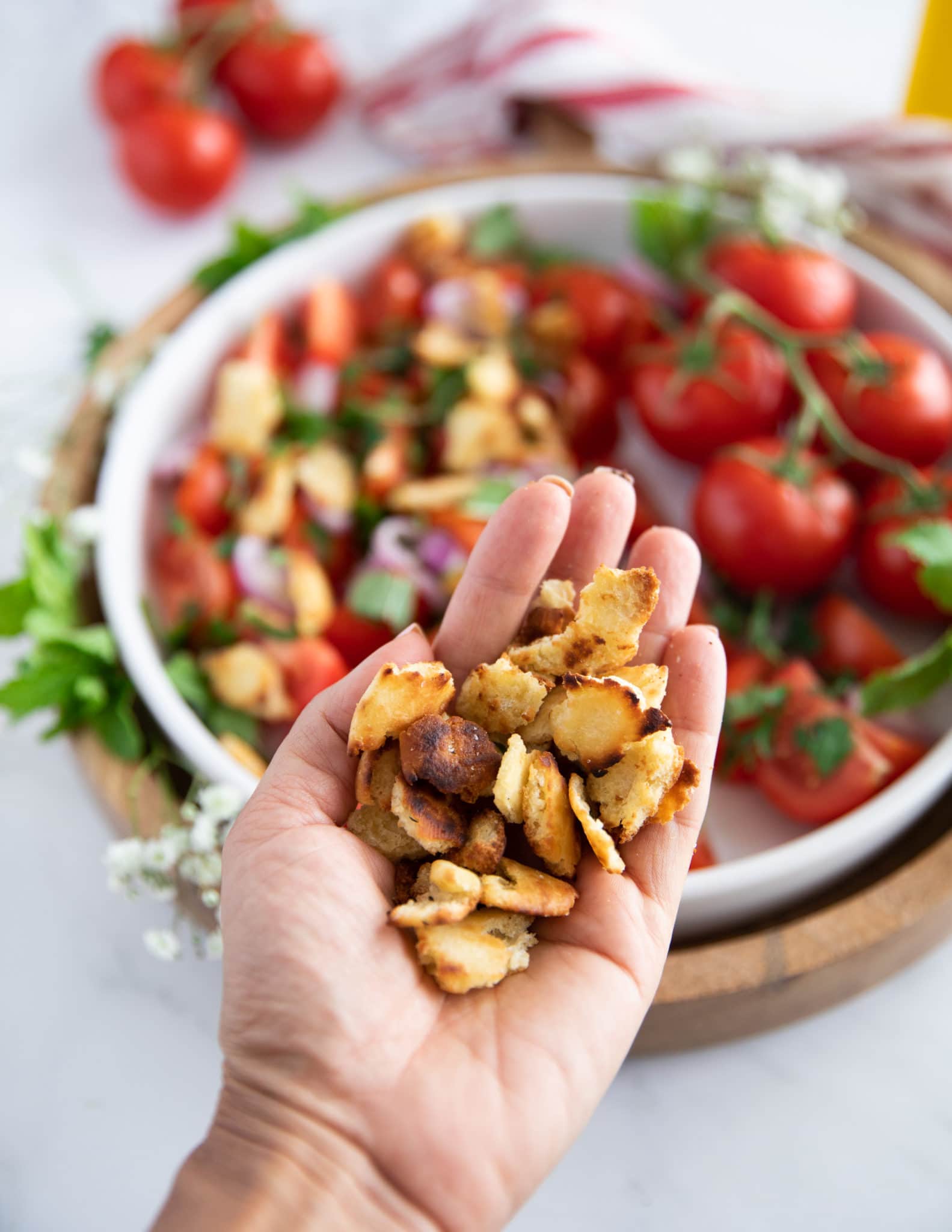 A hand holding the toasted bread chunks ready to toss into the salad