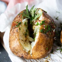 Close up of air fryer baked potato sliced and seasoned with a sprig of rosemary